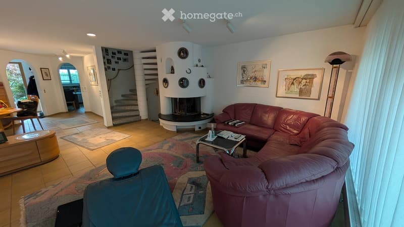 Living room with a red leather sofa, coffee table, fireplace, and large windows. The room features a mix of modern and classic decor, including artwork and a staircase leading to another level.