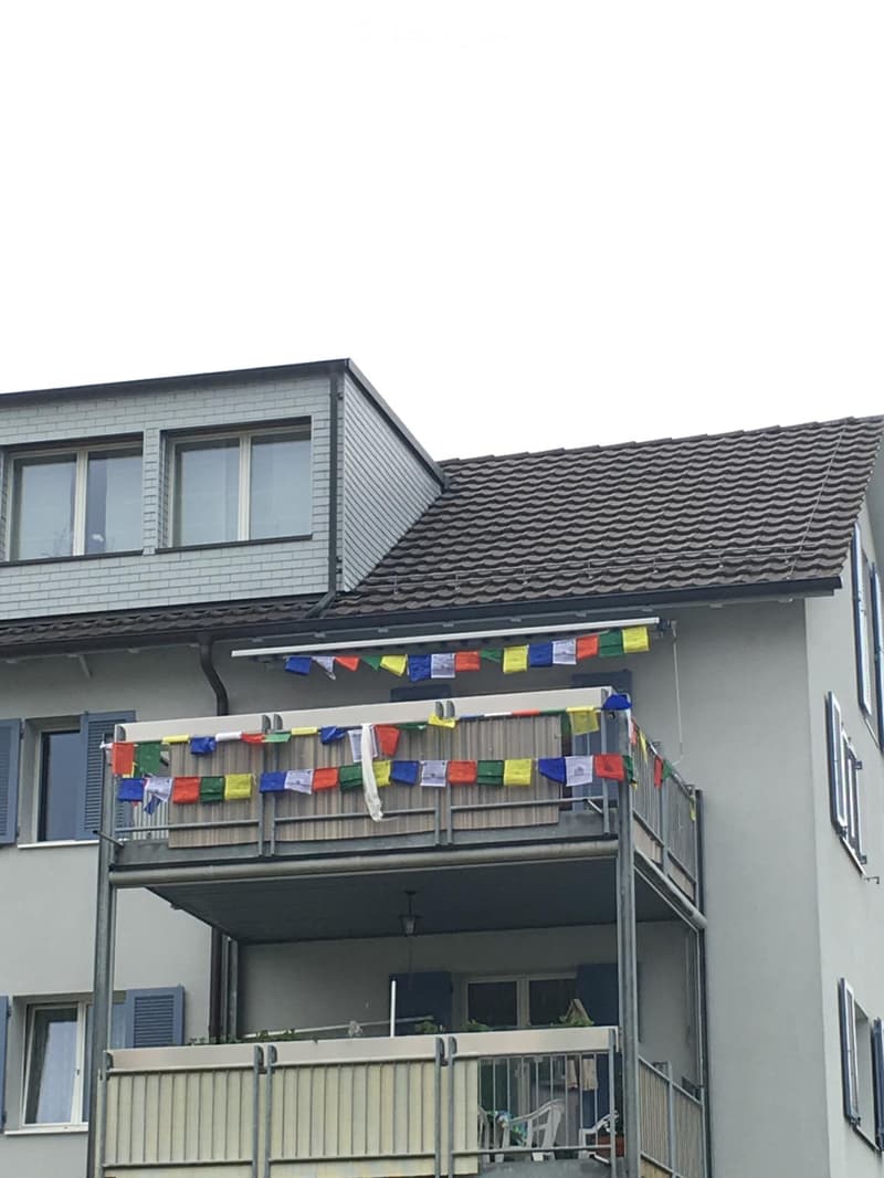 Multi-story residential building with balconies, colorful prayer flags, and visible windows.