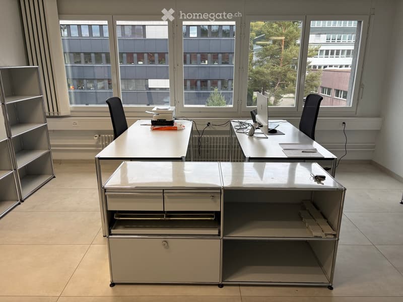 Office space with two desks, chairs, laptops, keyboards, and a metal shelving unit with drawers.