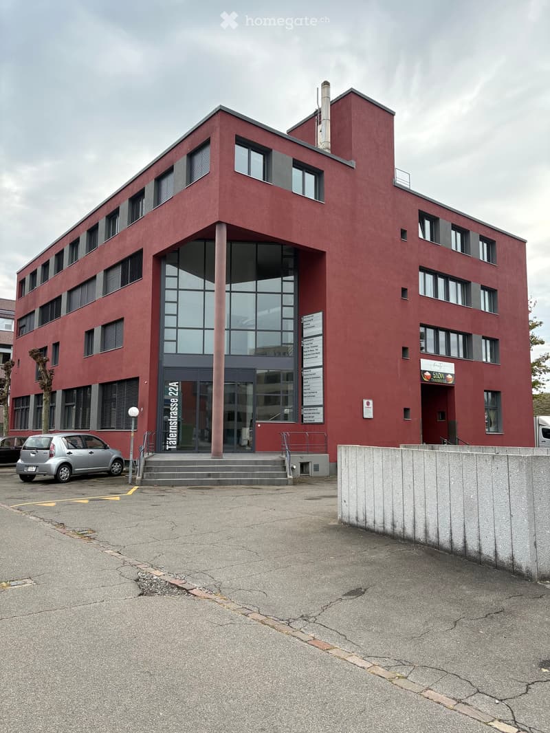 Red brick building with large windows and a modern design, featuring a sign for "SLOV THAMISS" and a parking area.