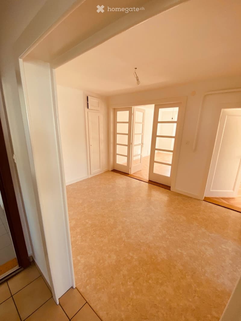 Empty hallway with beige tiled floor, white walls, and multiple doors including a sliding glass door leading to another room.