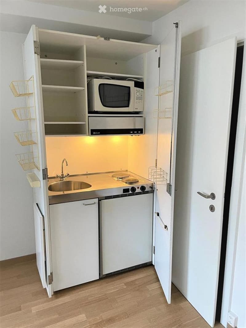 Compact kitchen with white cabinets, microwave, stove, sink, and built-in storage shelves.