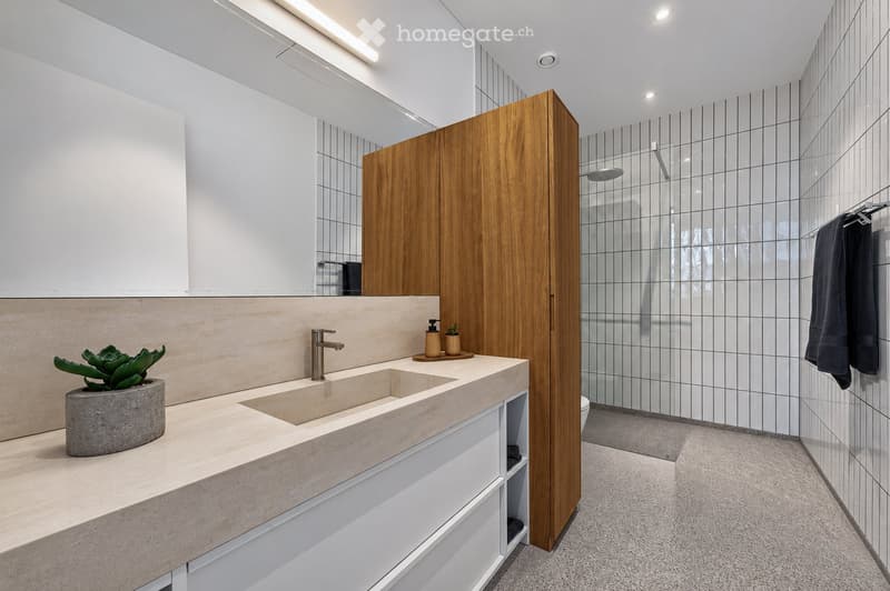 Modern bathroom with a double sink, wooden cabinet, large mirror, and a glass-enclosed shower area.