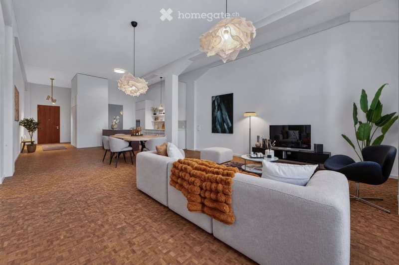 Modern living room with a grey sectional sofa, coffee table, ottoman, dining area with chairs and table, pendant lights, floor lamp, television, and decorative plants.