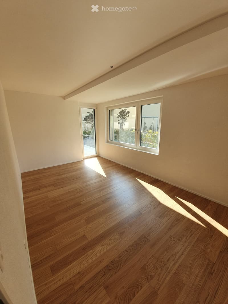 Empty room with wooden flooring, white walls, and large windows with a sliding door leading outside.