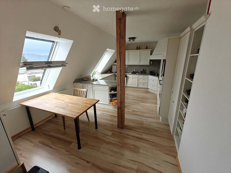 Bright kitchen with wooden flooring, white cabinets, a central wooden dining table with a chair, and large skylight windows offering a view.