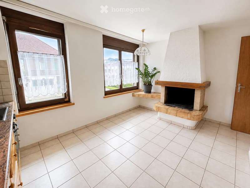 Living room with tiled floor, fireplace, potted plant on mantel, large windows with white curtains, and a chandelier.