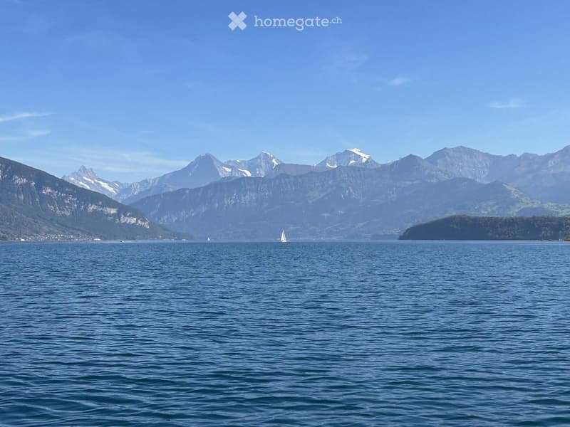 A serene lake view with snow-capped mountains in the background and a sailboat on the water.
