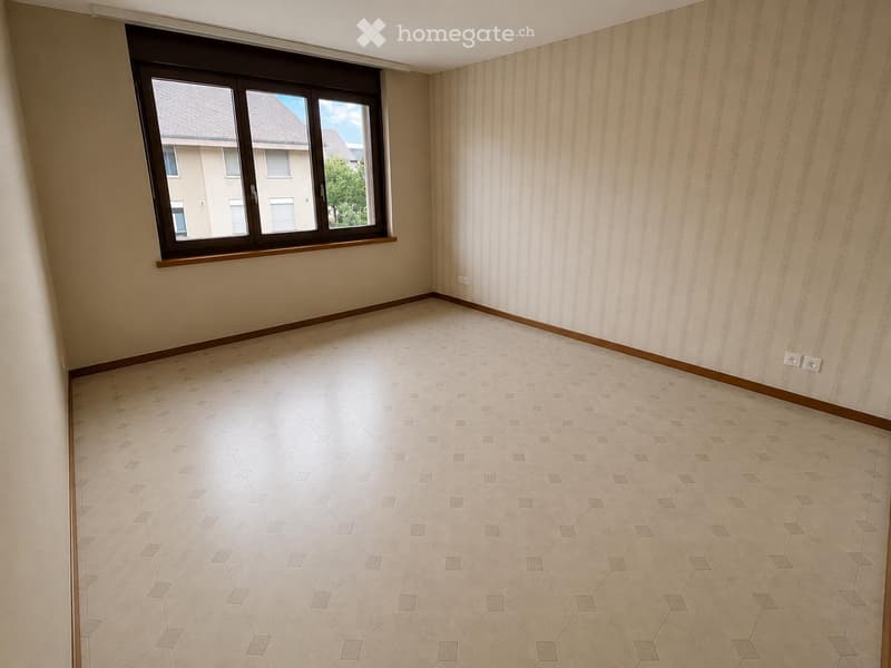 Empty room with beige tiled floor, light-colored striped wallpaper, and a large window with wooden frame and white trim.