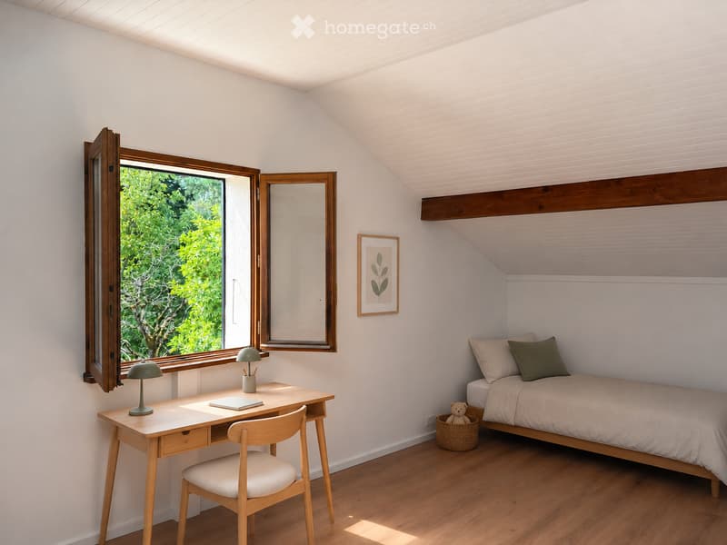 Cozy bedroom with a slanted ceiling, wooden bed, desk, chair, and a large window offering a view of greenery.