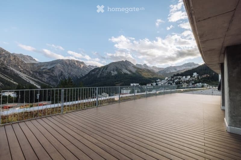 Wooden deck terrace with metal railing, overlooking a scenic mountain range and town below.