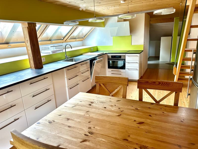 Modern kitchen with white cabinets, dark countertops, a wooden dining table, and two wooden chairs. Features a sink, faucet, and built-in oven.