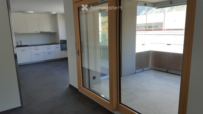 Modern kitchen with white cabinets, a sink, and an oven, connected to a tiled balcony area through large glass doors.
