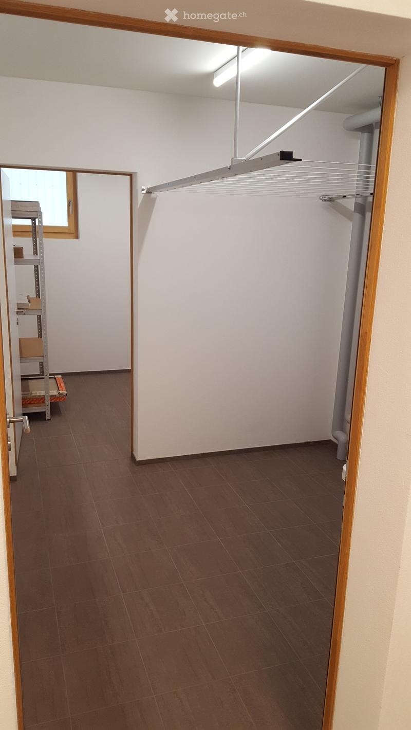 Empty hallway with tiled floor, white walls, and a clothes rack attached to the wall. A door leads to another room with a metal shelving unit visible.