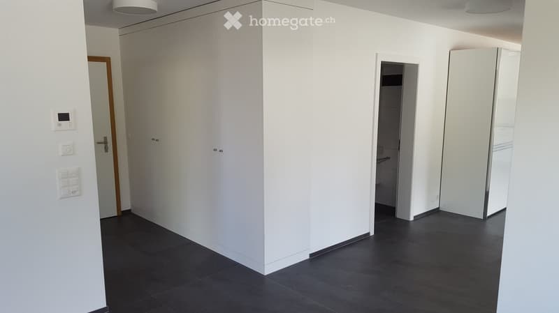 Empty room with white walls, dark tiled floor, and built-in white closet. A small bathroom is visible through an open doorway.