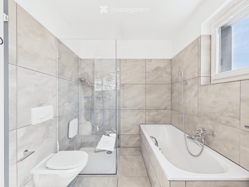 Modern bathroom with a bathtub, toilet, glass-enclosed shower, and tiled walls.