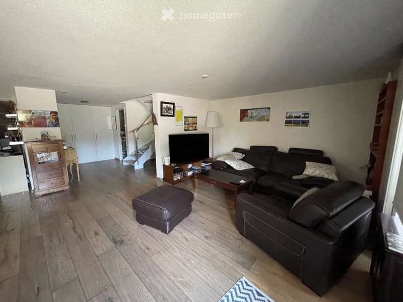 Modern living room with dark leather sofa, coffee table, ottoman, armchair, TV stand, floor lamp, and cabinet. Wooden flooring and white walls.