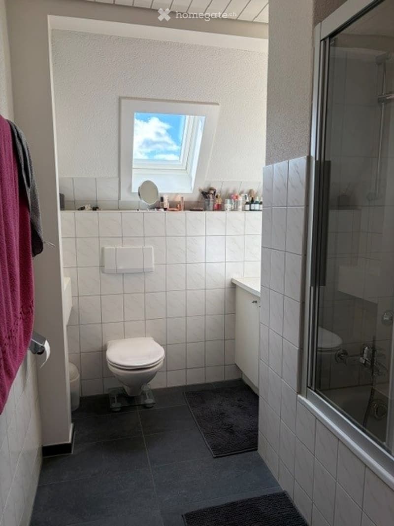 Modern bathroom with white tiles, a toilet, a shower, a mirror, and a small window with blinds.