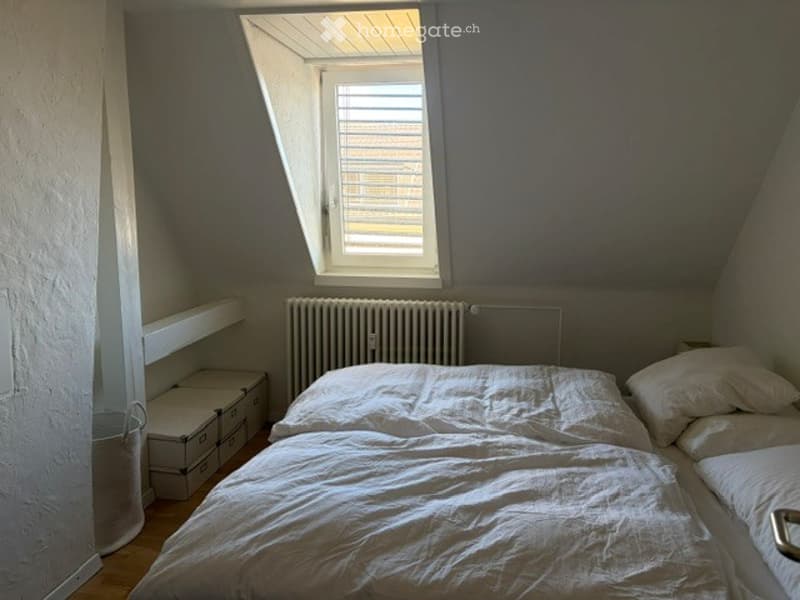Cozy attic bedroom with a single bed, white linens, built-in shelves, radiator, and storage boxes.