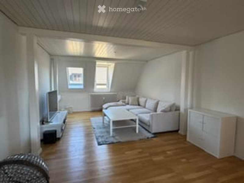 Bright living room with wooden flooring, white walls, large windows, grey sofa, white coffee table, TV stand, and cabinet.