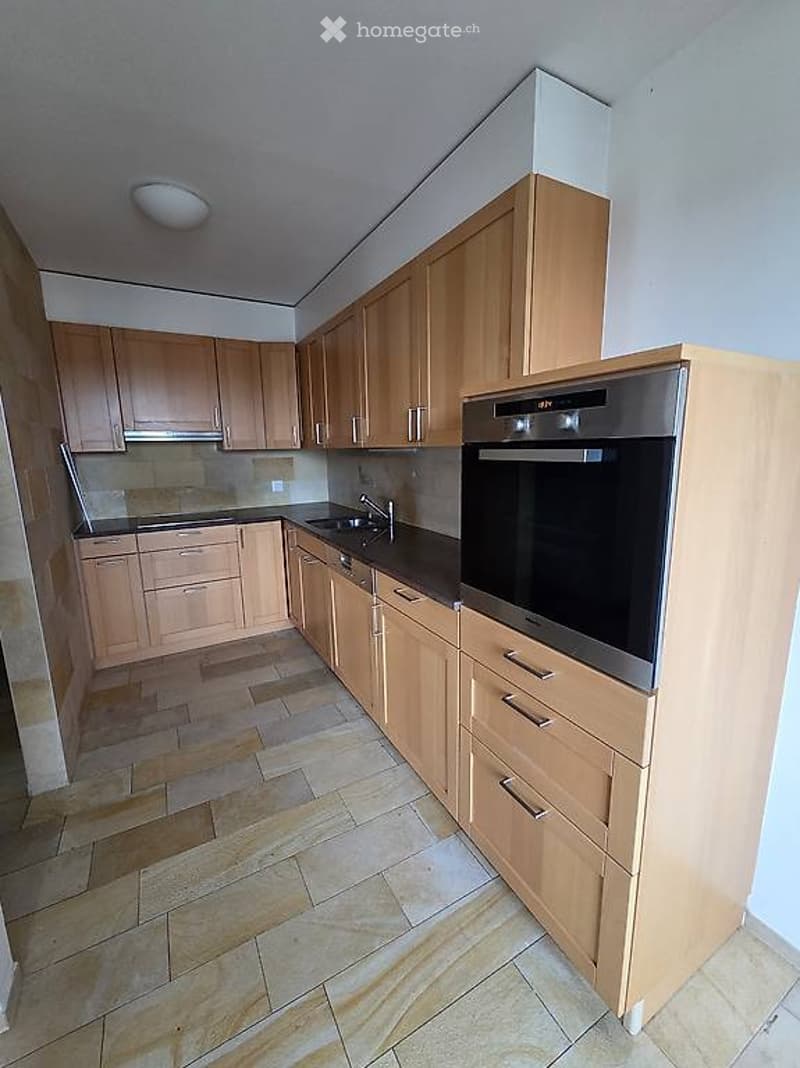 Modern kitchen with light wooden cabinets, stainless steel oven, sink, and faucet. Tile flooring and white walls.