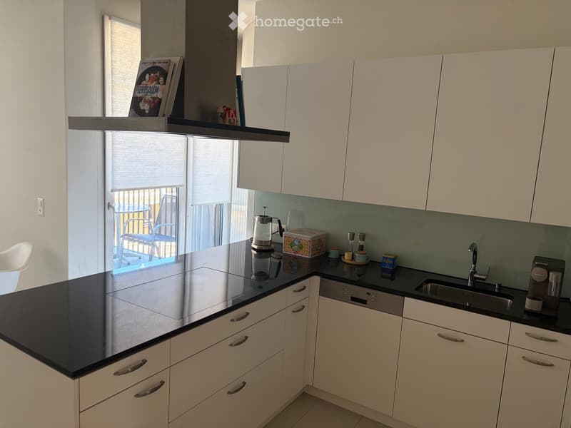 Modern kitchen with white cabinets, black countertops, stainless steel appliances, and a coffee maker on the counter.