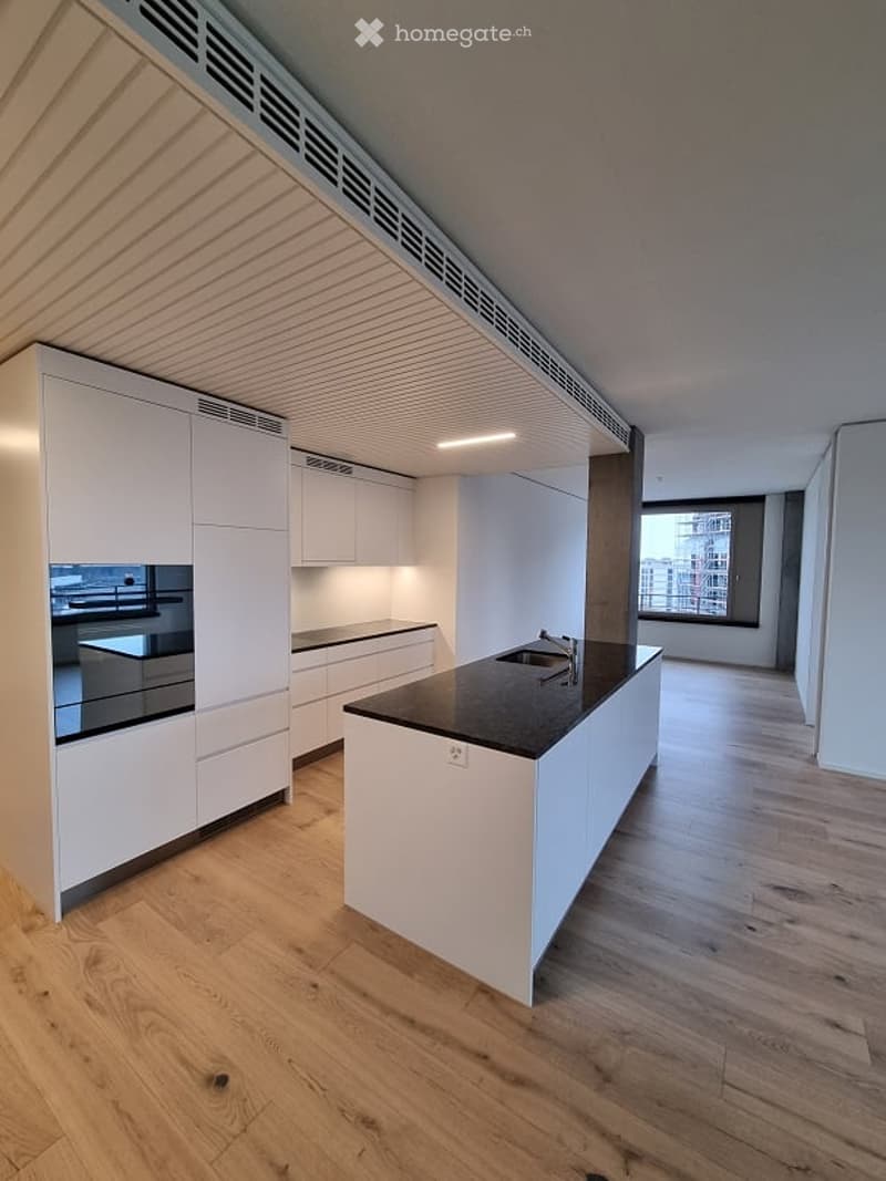 Modern kitchen with white cabinets, a central island, and a black countertop. The floor is made of light wood, and there is a large window providing natural light.