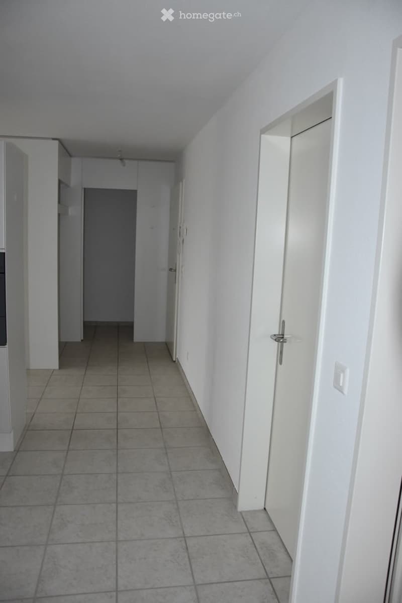 Empty hallway with tiled floor, white walls, and several closed doors.