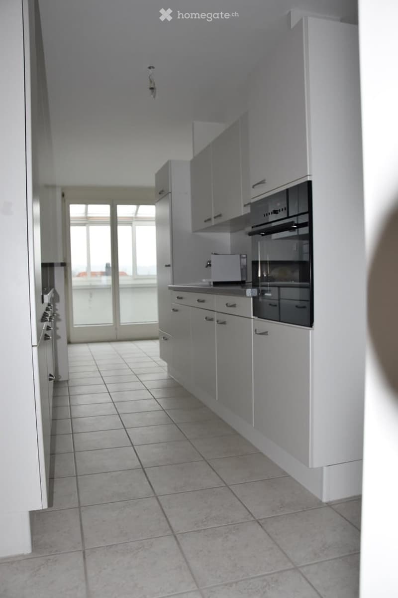 Modern kitchen with white cabinets, tiled floor, and built-in appliances including an oven, microwave, and refrigerator. Large window provides natural light.