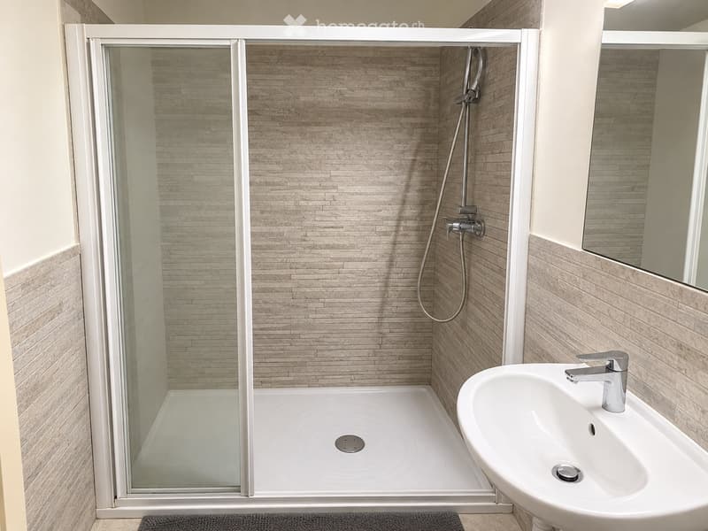 Modern bathroom with a glass-enclosed shower, a white sink with a chrome faucet, and beige tiled walls.