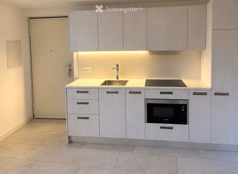 Modern, compact kitchen with light-colored cabinets, a sink, a stove, and a microwave. The space features a clean, minimalist design with a warm LED under-cabinet light.