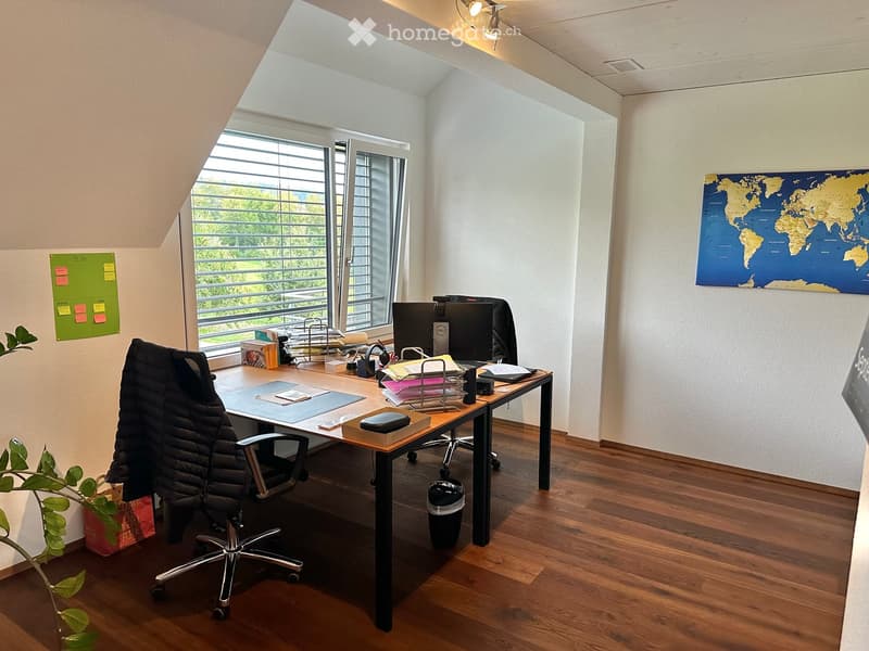 Office space with wooden flooring, large window with blinds, desk with computer, chair, world map on wall, and whiteboard.