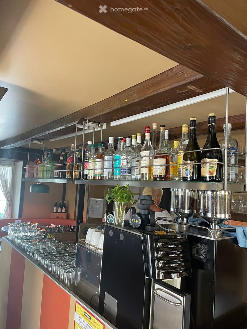 A well-organized bar area with a coffee machine, cup dispenser, bottle rack, and glassware neatly arranged on shelves and counters.