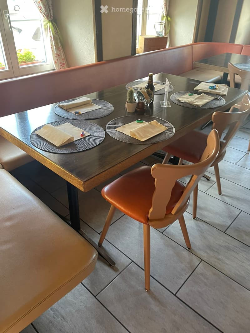 A modern dining area with a long wooden table, leather bench seating, and a single wooden chair. The table is set with plates, napkins, and a small cactus in a pot.