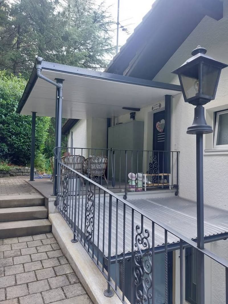 Balcony with metal railing, two chairs, small table, and decorative items.