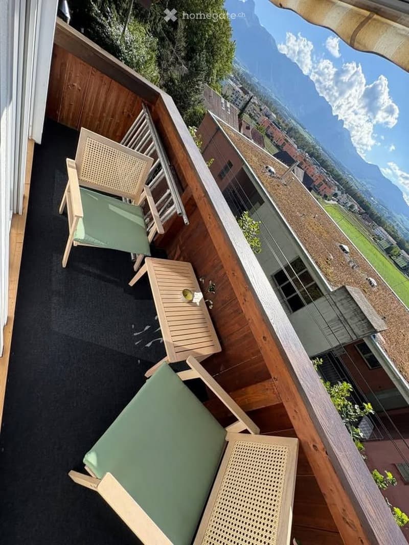Balcony with wooden floor, glass railing, two chairs, and a small table with a candle.