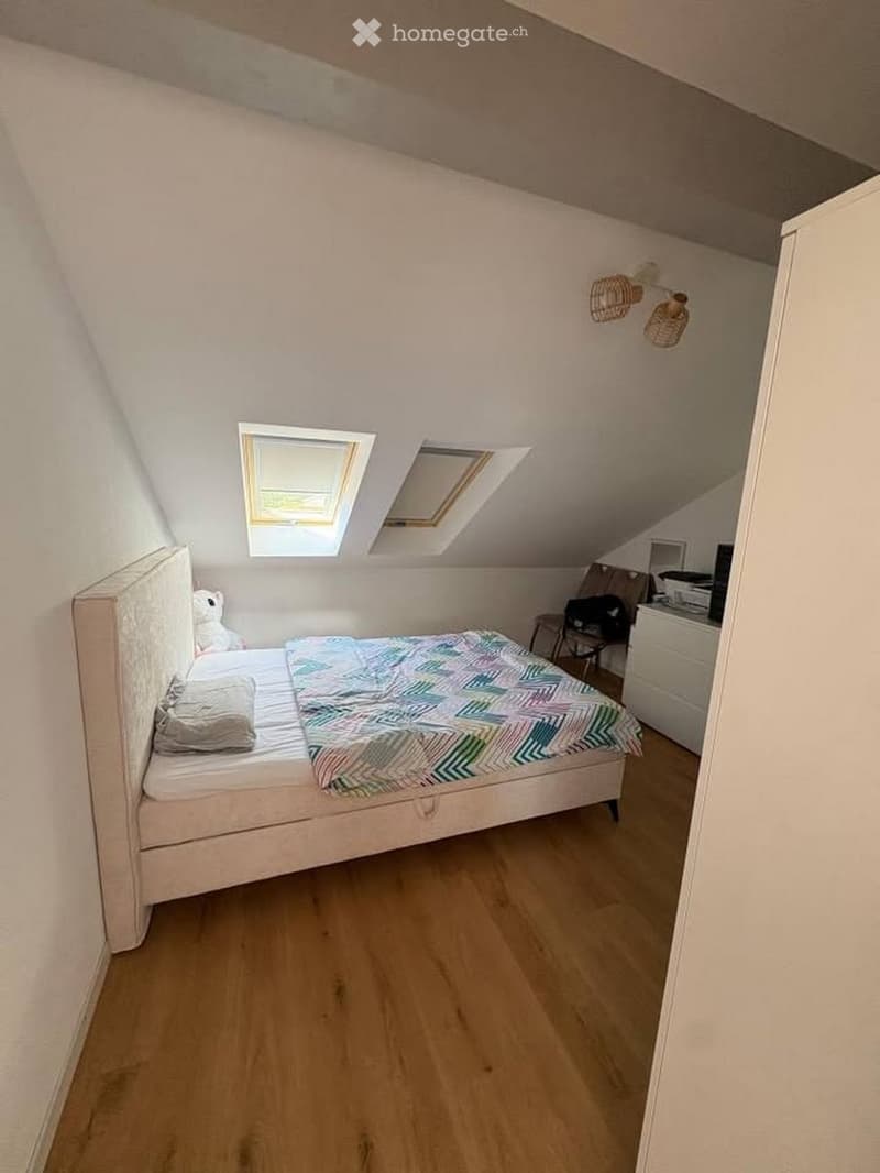 Cozy attic bedroom with wooden flooring, slanted ceilings, skylight windows, and a neatly made bed with colorful bedding.