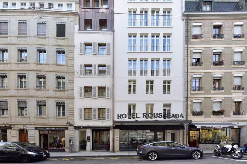 A row of multi-story buildings with classic European architecture, including a hotel sign reading "HOTEL ROUSSEAU" and several storefronts along the ground level.