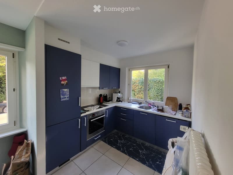 Modern kitchen with dark blue cabinets, white countertops, and stainless steel appliances. Features a refrigerator, oven, sink, and various kitchen items on the counter.
