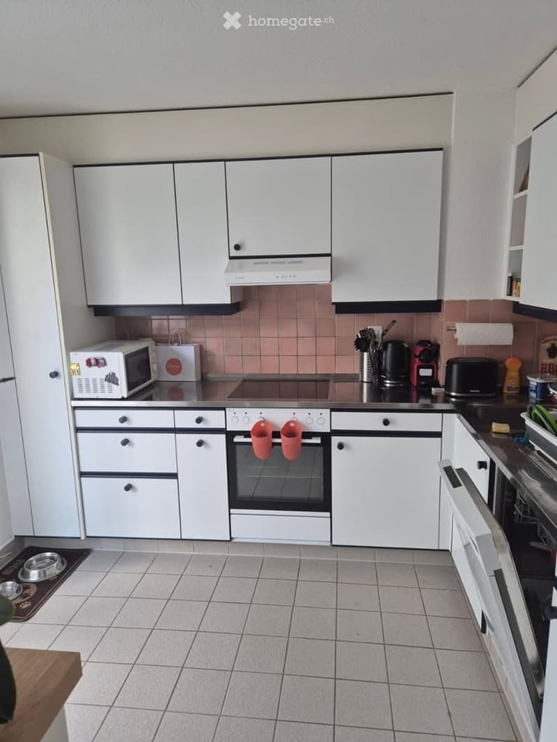 Modern kitchen with white cabinets, tiled backsplash, microwave, oven, coffee maker, toaster, and various kitchen utensils.