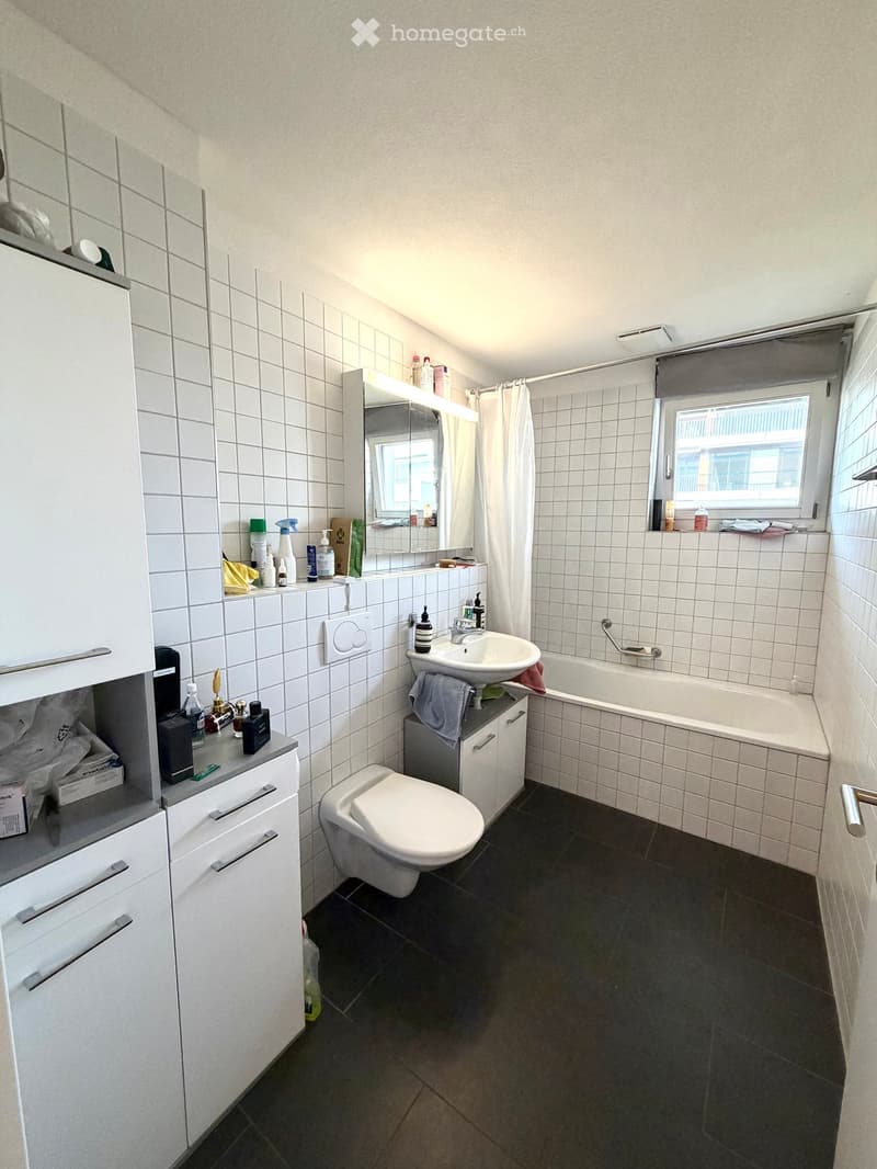Bathroom with white tiled walls, dark tiled floor, toilet, sink, bathtub, mirror, and cabinet.