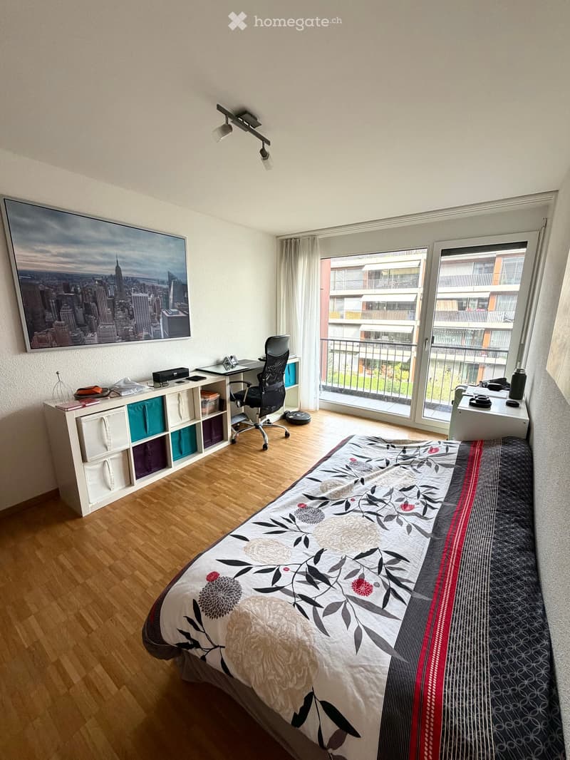 Bedroom with a bed, desk, chair, shelf, and large windows opening to a balcony.