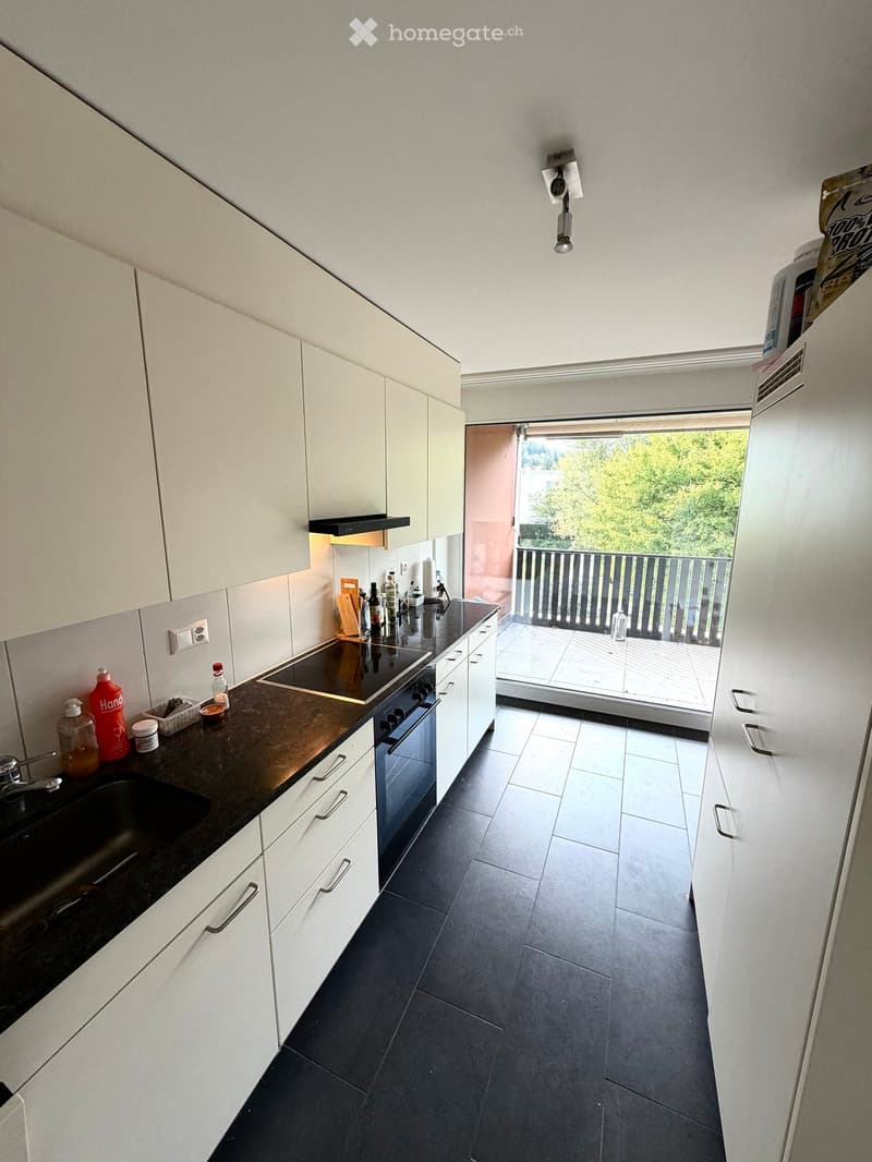 Modern kitchen with white cabinets, black countertop, stainless steel appliances, and a view to a balcony.