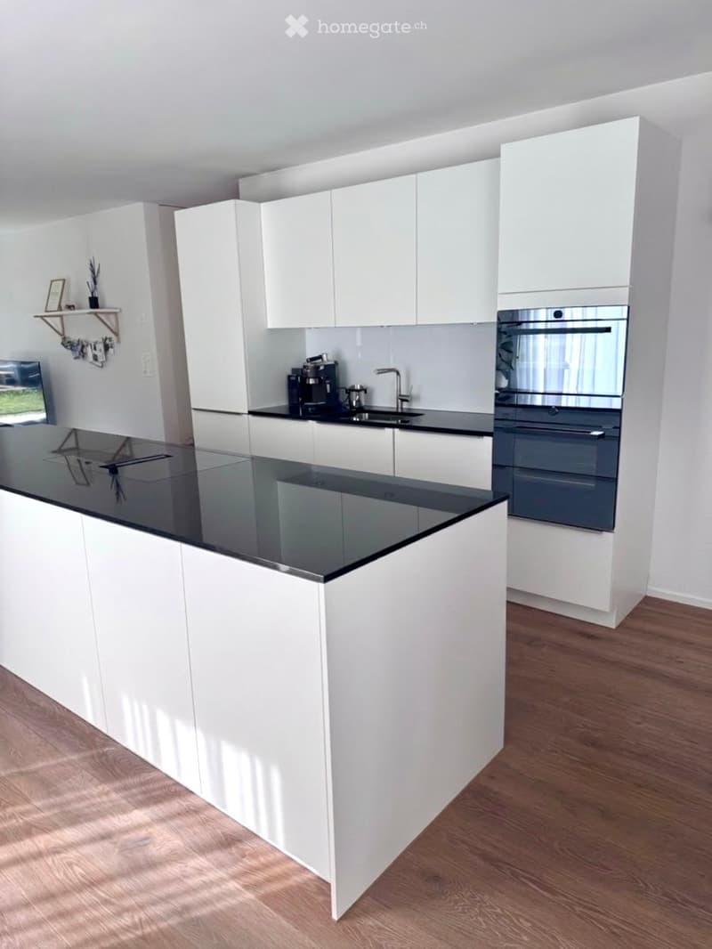 Modern kitchen with white cabinets, black countertops, a central island, and stainless steel appliances including an oven and coffee maker.