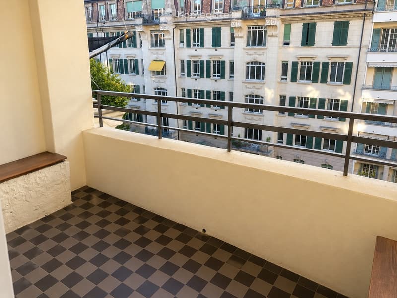 Balcony with checkered tile flooring, metal railing, and a view of surrounding buildings with green shutters.
