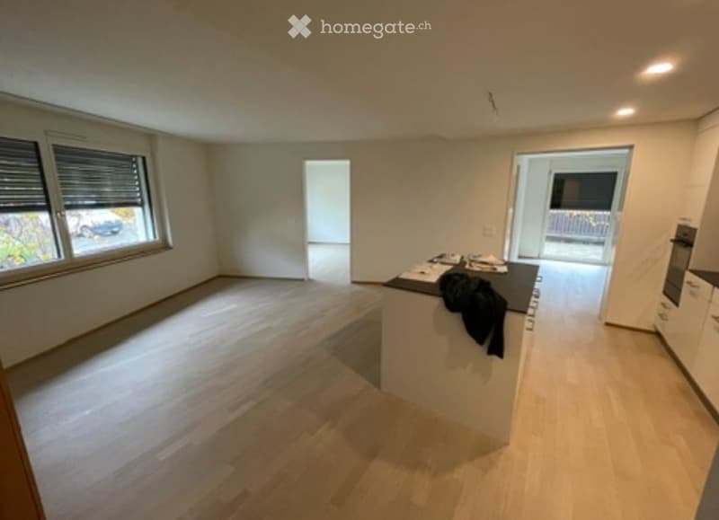Empty kitchen with light wooden flooring, white cabinets, and a black countertop. A doorway leads to a balcony area.