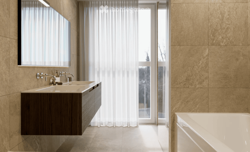 Modern bathroom with a double sink vanity, large mirror, bathtub, and sheer curtains covering a window.