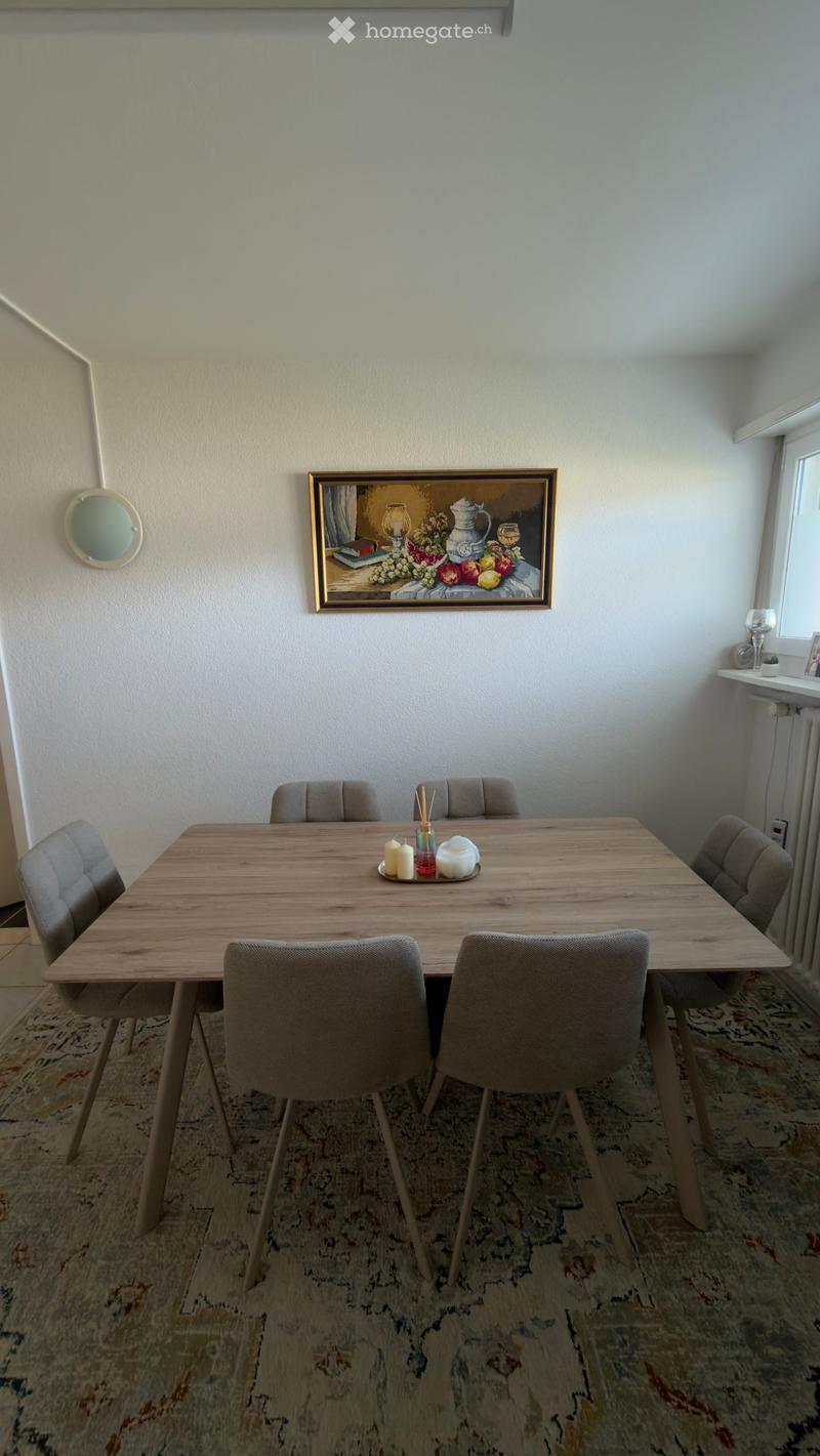Dining room with a wooden dining table, six chairs, a teapot, candles, and a framed painting on the wall.