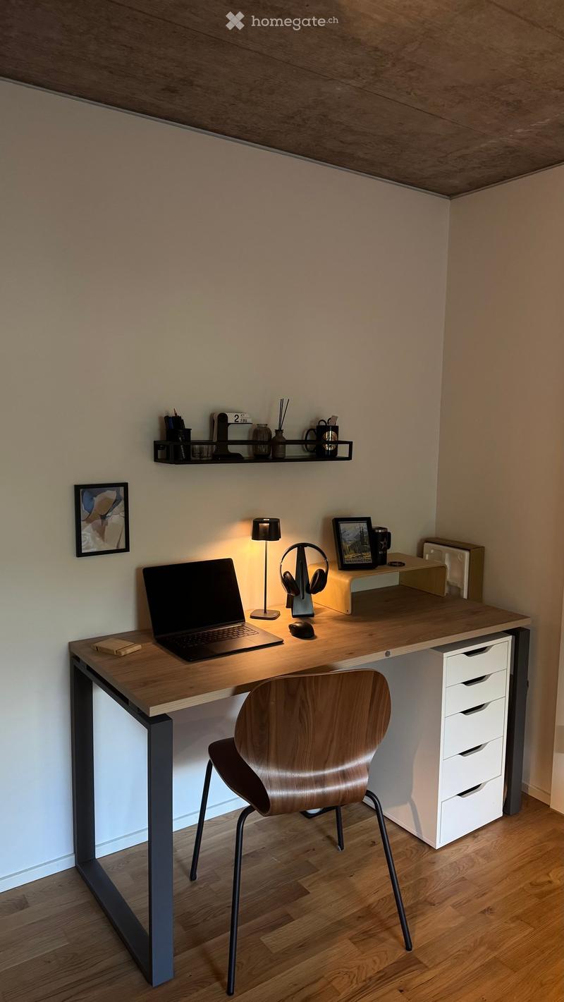 A modern, minimalist desk setup with a wooden desk, ergonomic chair, laptop, mouse, lamp, headphones, and decorative items on shelves and the desk surface.