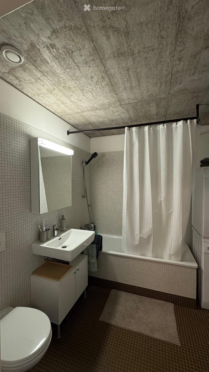 Modern bathroom with a white sink, toilet, bathtub, and mirror. Features a shower curtain, tiled walls, and a small cabinet under the sink.